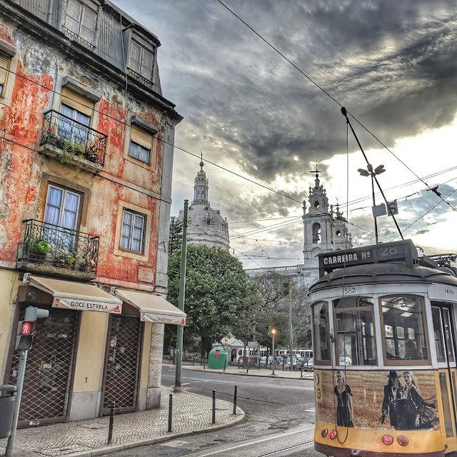 Yellow street car in Lisbon as it passes an old red building