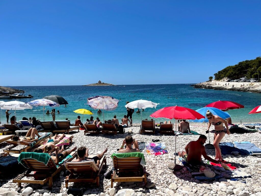 Rocky beach with umbrellas and sunbathers in Hvar, Croatia