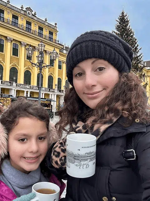 Little girl and mother posing for a photo with mugs at an Austrian Christmas Market at Schonbrunn Palace