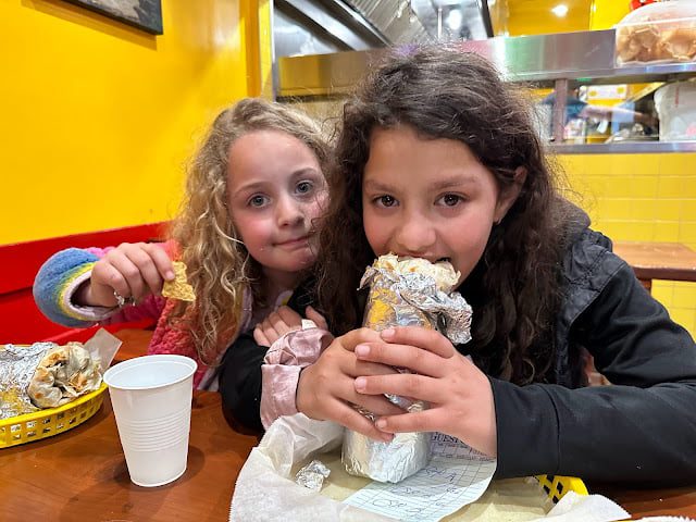 Great food is a highlight of visiting Northern California with kids. Two girls eat burritos at Taqueria Cancun in San Francisco