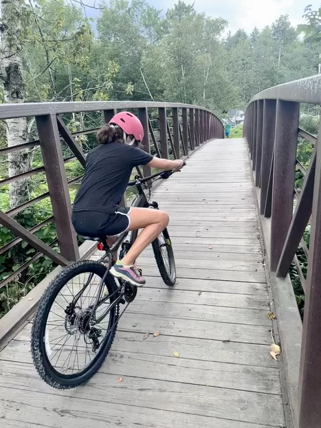 Little girl in pink helmet riding bike over bridge in Stowe, VT
