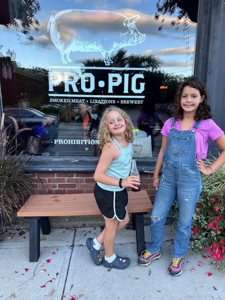 Two girls posing in front of Pro Pig sign on window at Prohibition Pig in Waterbury, VT