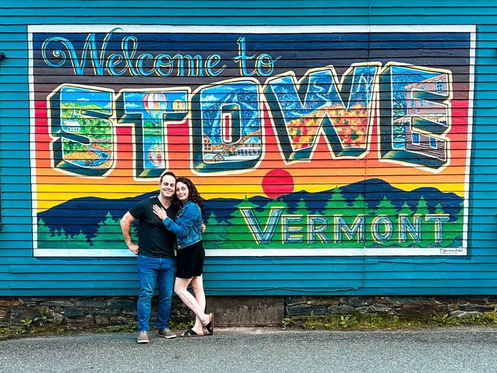 Man and woman from Adventurous Tastes in front of Stowe sign on a wall in Vermont