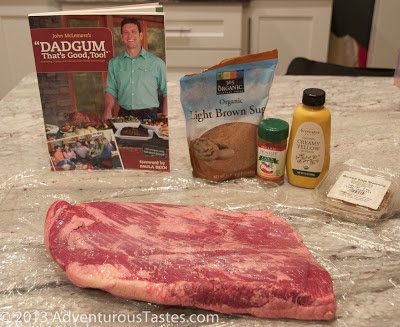Ingredients for smoking meat on the masterbuilt smoker - raw brisket, brown sugar, mustard, and the dadgum cookbook