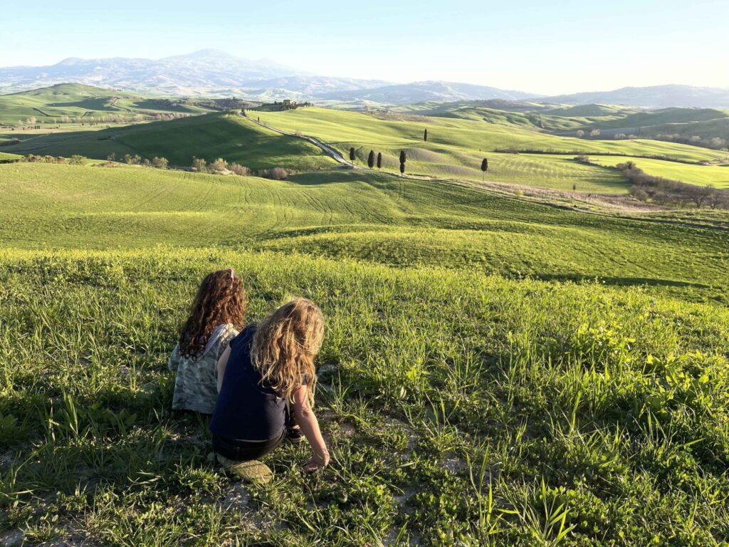 Tuscany with kids highlights - Two girls taking in the view of rolling green hills and cypress trees. Tuscany is one of the best places to consort in Europe for families