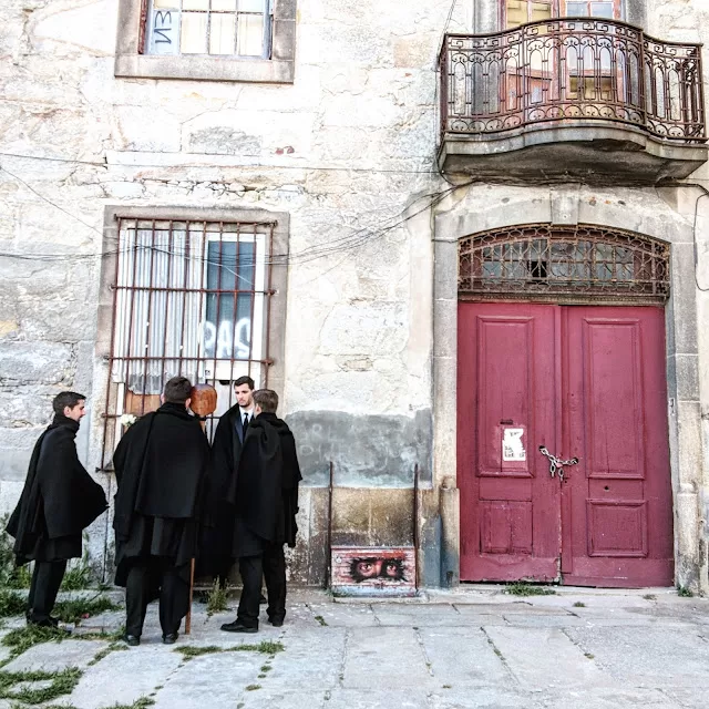 Black cloacked students on a street in Porto,Portugal, next to a red door.