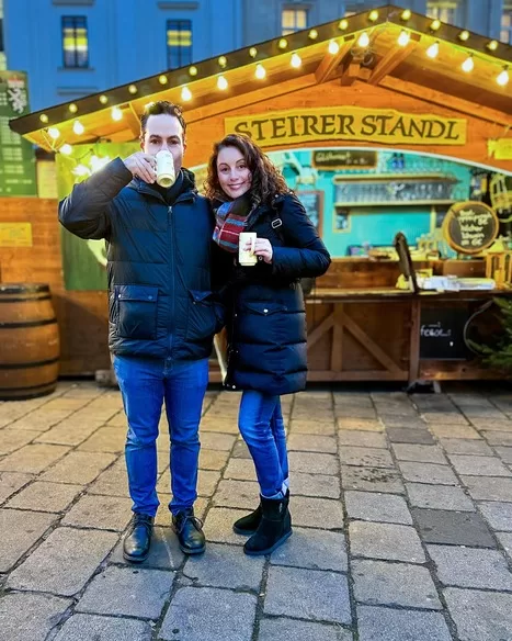Man taking a sip of gluhwein with his wife by his side at Am Hof one of many lovely Austrian Christmas markets in Vienna