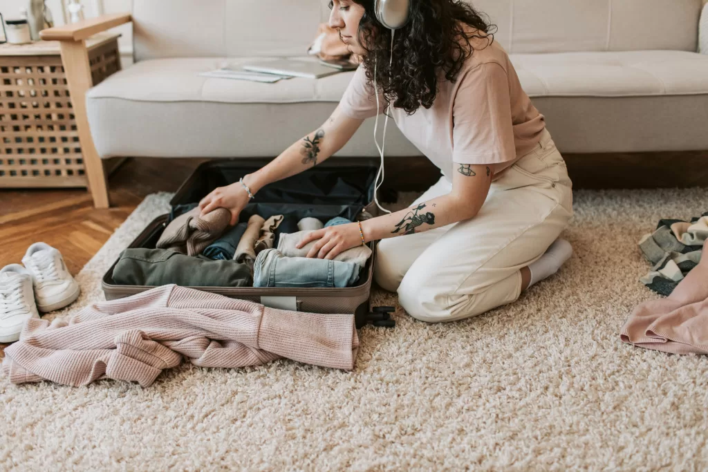 Woman wearing headphones as she packs her travel wardrobe in a suitcase Photo by Vlada Karpovich: https://www.pexels.com/photo/a-woman-listening-on-her-headphones-while-packing-her-clothes-7365331/