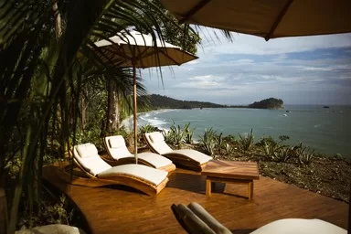 Arenas Del Mar - one of the besrt resorts to visit in Costa Rica with Kids. Loungers by the pool looking out over the tropical beach near Manuel Antonio