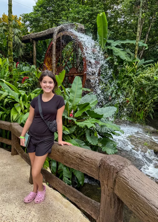 Little girl with dark hair posing in front of lush foliage and a water feature at Los Lagos resort in La Fortuna, Costa Rica