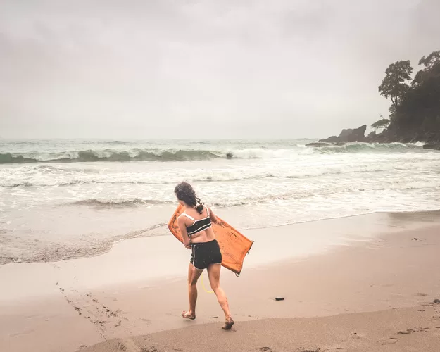 A visit to Costa with Kids is full of adventures. A girl walks into the ocean with a body board near Manuel Antonio Park in Costa Rica