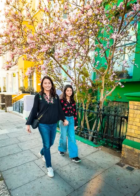 Mother and daughter walking down a Notting Hill London street in springtime. They're holding hands and the mother wears Veja shoes and a Clare V cross body bag, both perfect travel gifts for moms.