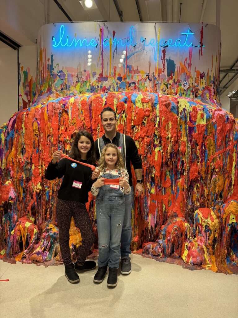 Two girls (a ten-year-old with slime in her hands and an eight-year-old) and there father was standing behind them. Behind all of them there was a wall covered in slime.