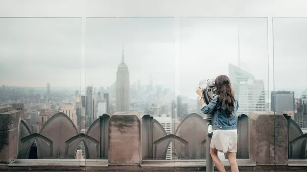 Visiting a rooftop for the view is one of the best things to do in New York City with a teenager | Teenage girl looking through binoculars from a rooftop