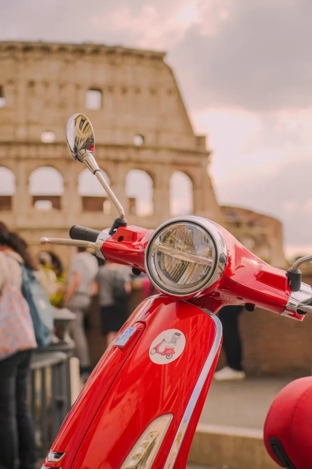 red Vespa scooter with colosseum in rome backdrop