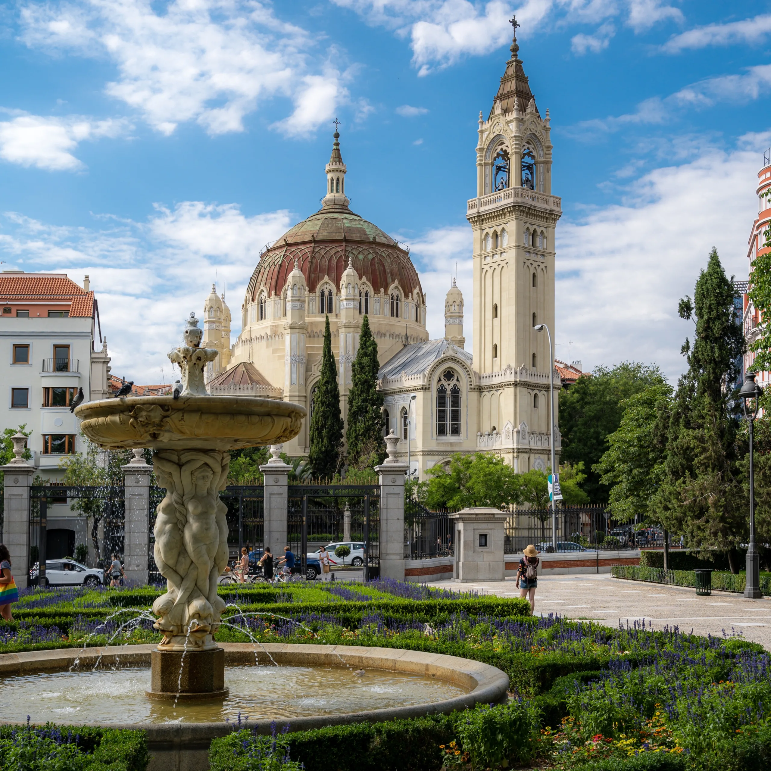A fountain and garden with a backdrop of beautiful buildings in Madrid, Spain.